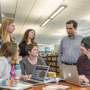 An LIS instructor has a conversation with a group of students in the library