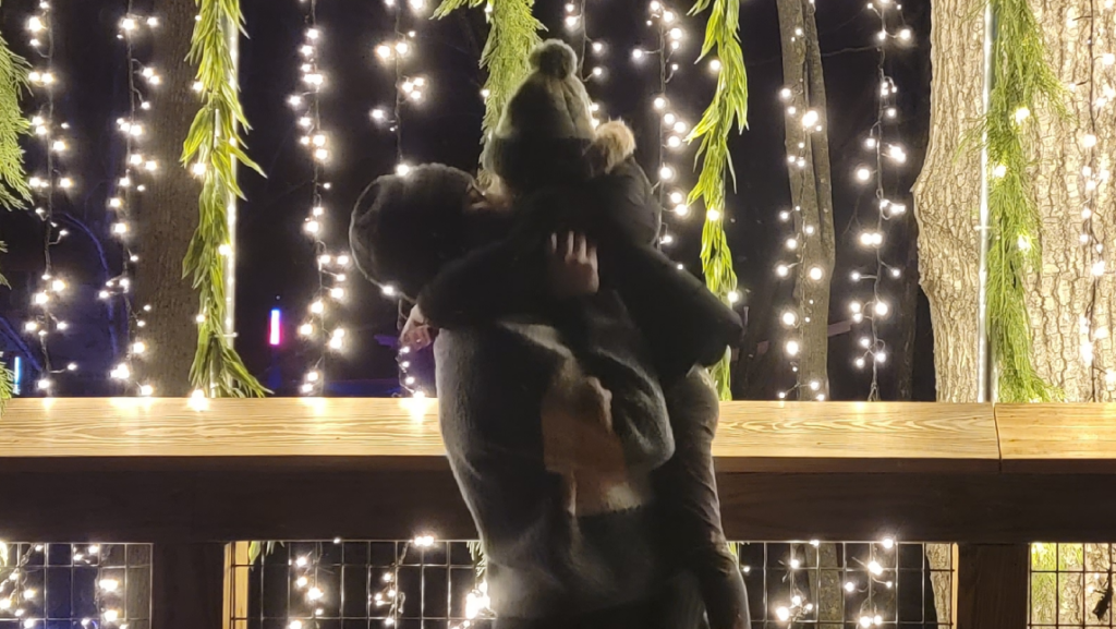 Melissa Carmona holds up her child in front of strings of lights