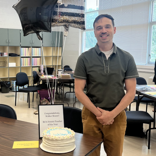 Walter Moore stands next to a celebration cake and balloons after being named 2023-24 Rockingham County Schools Teacher of the Year