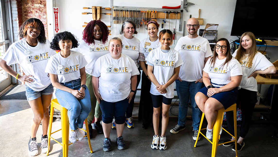 A group of people wearing shirts that say "Create" gathered around workshop tools