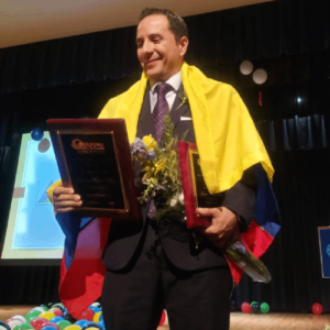 Jhonatan Marin Mesa, wrapped in a Colombian flag, holds his Guilford County Schools Teacher of the Year plaque