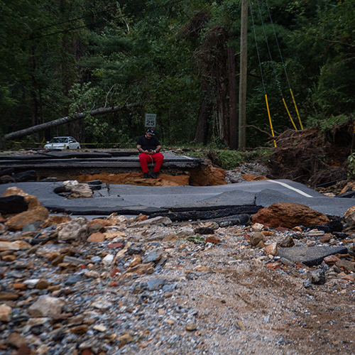 A man sits where a road has been washed out