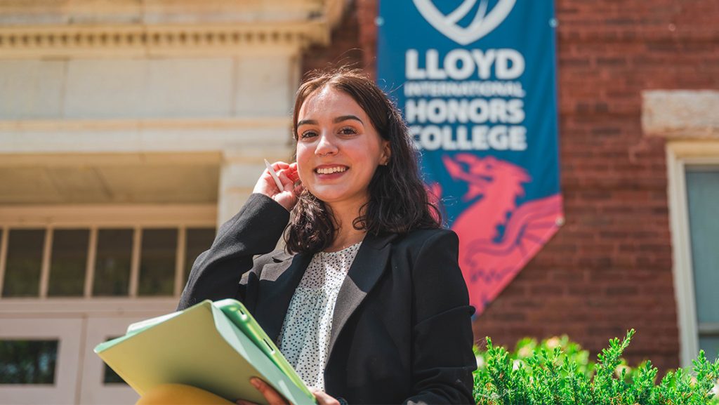 Natalia Fagundez stands in front of a campus building with a Lloyd International Honors College banner hanging on it