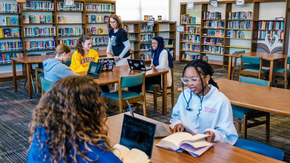students sitting in a library with laptops and books