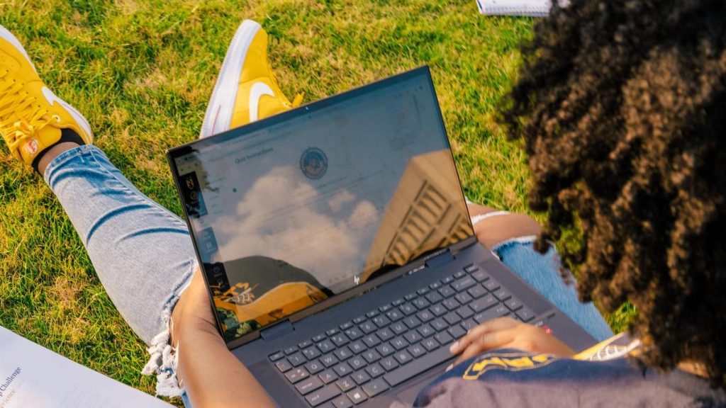 student sits outside on grass with a laptop in their lap