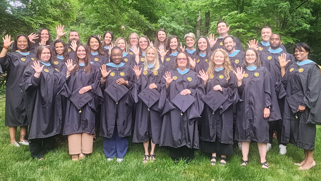 Graduating members of the PPEERS cohort stand in their caps and gowns in front of trees