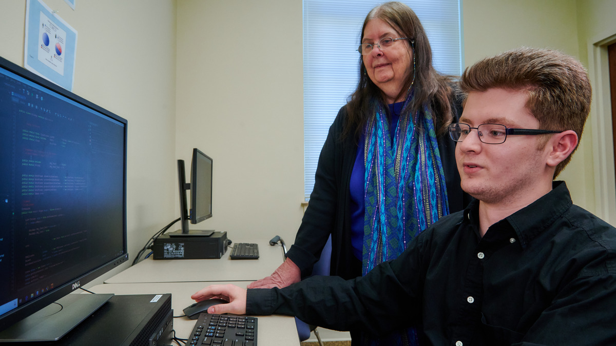 Information science student working with data and code alongside faculty support in a computer lab