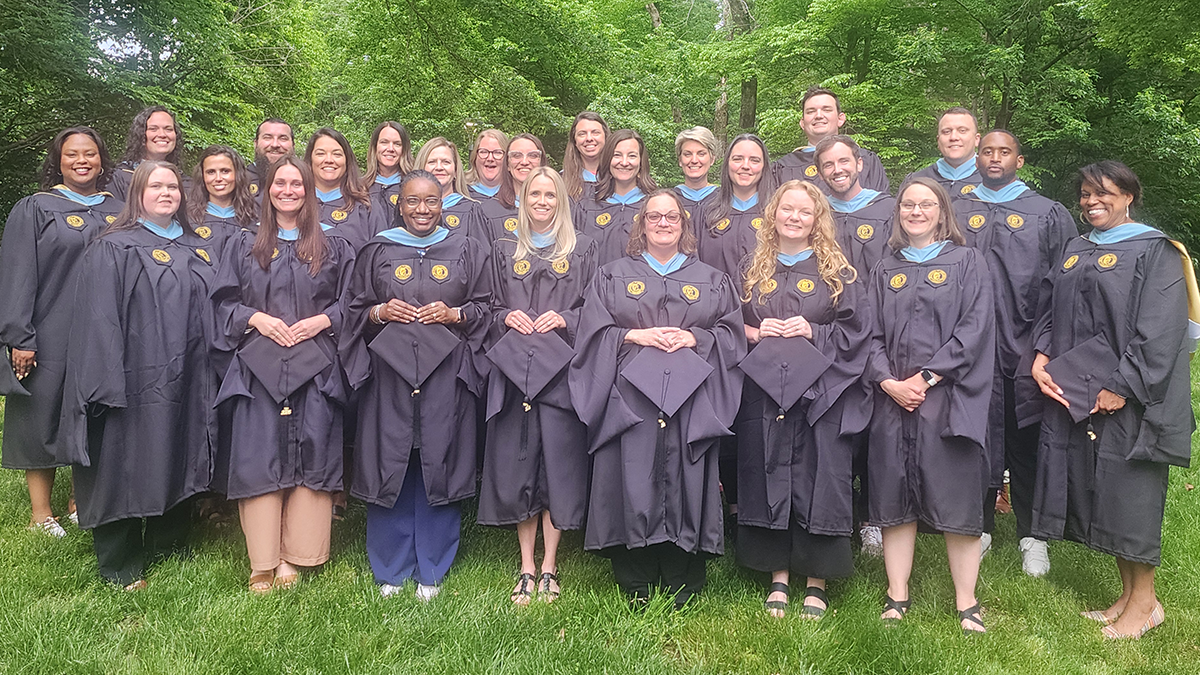 Graduating members of PPEERS cohort five stand in their caps and gowns in front of trees