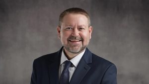 Dr. Charles Perkins wearing a suit and tie in front of a gray background