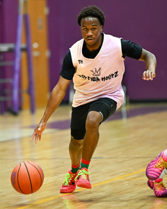 Cameron Davis dribbles a basketball during an indoor game, wearing a light pink Top Tier Hoopz jersey, black shorts, and bright pink-and-green shoes.