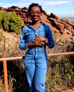 Adrianna Fields smiles in a denim jumpsuit at a rocky outdoor overlook.